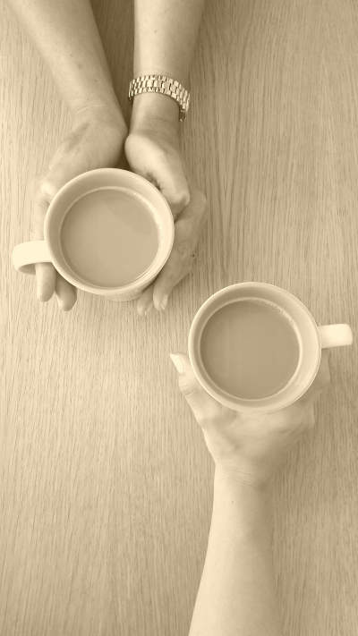 Image was here which showed from above a table-top on which are the arms and the hands of 2 people each holding coffee cups. The coffee cups are near each other, signifying a connection or conversation between the two people.