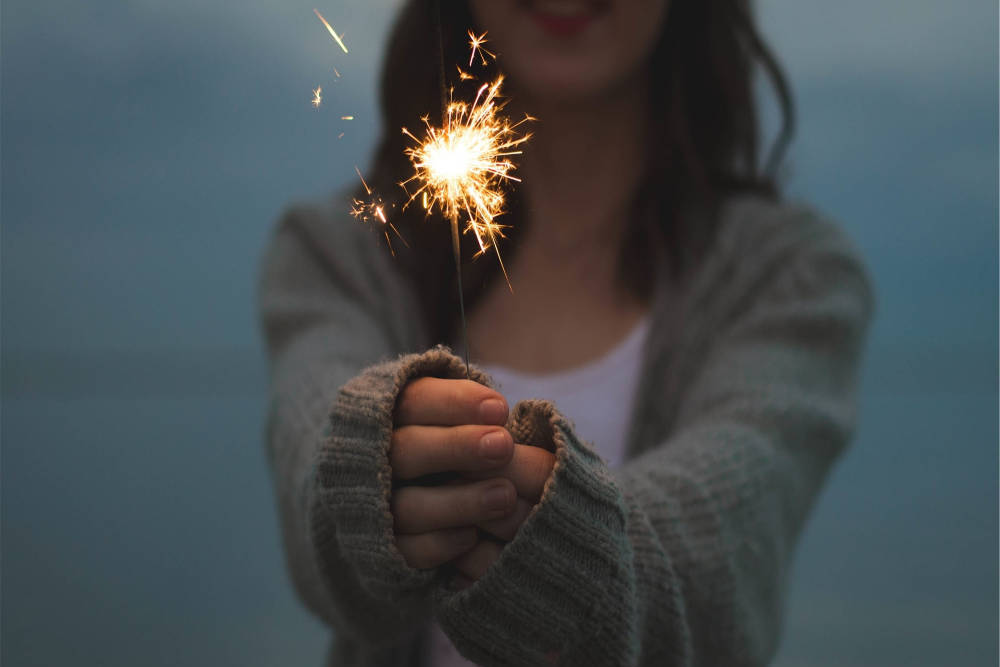image was here of a girl holding up a burning sparkler.