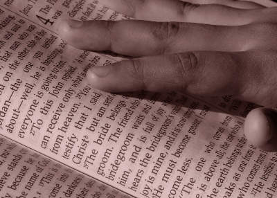 An image was here of a hand resting and pointing on a page with Bible verses.