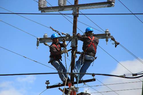 An image was here of two men with hard hats working together high up on an electric pole.