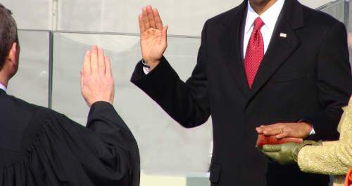 An image was here of a man with his right hand raised to give an oath, and his other hand on a Bible.  This man is standing in front of a judge wearing a black judge robe.