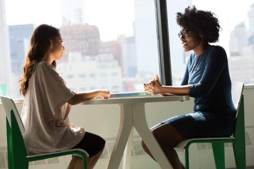 An image was here of two ladies sitting at a table facing each other near a window.  They seem to be enjoying conversation.